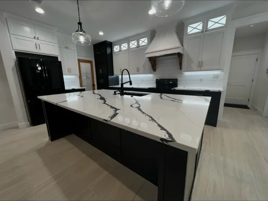 Custom kitchen with quartz waterfall island, white cabinetry, and a shiplap vent hood