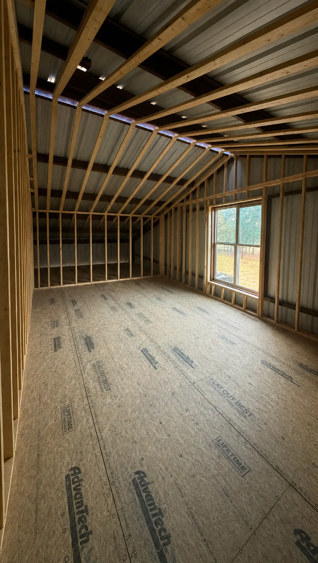Framed loft room inside a barndominium with vaulted rafters and a new window