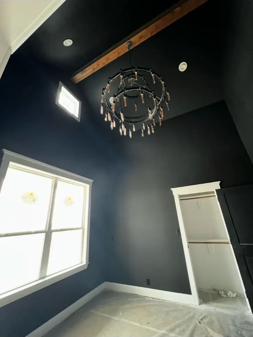 Vaulted room with navy accent walls, cedar beam, and a black ring chandelier