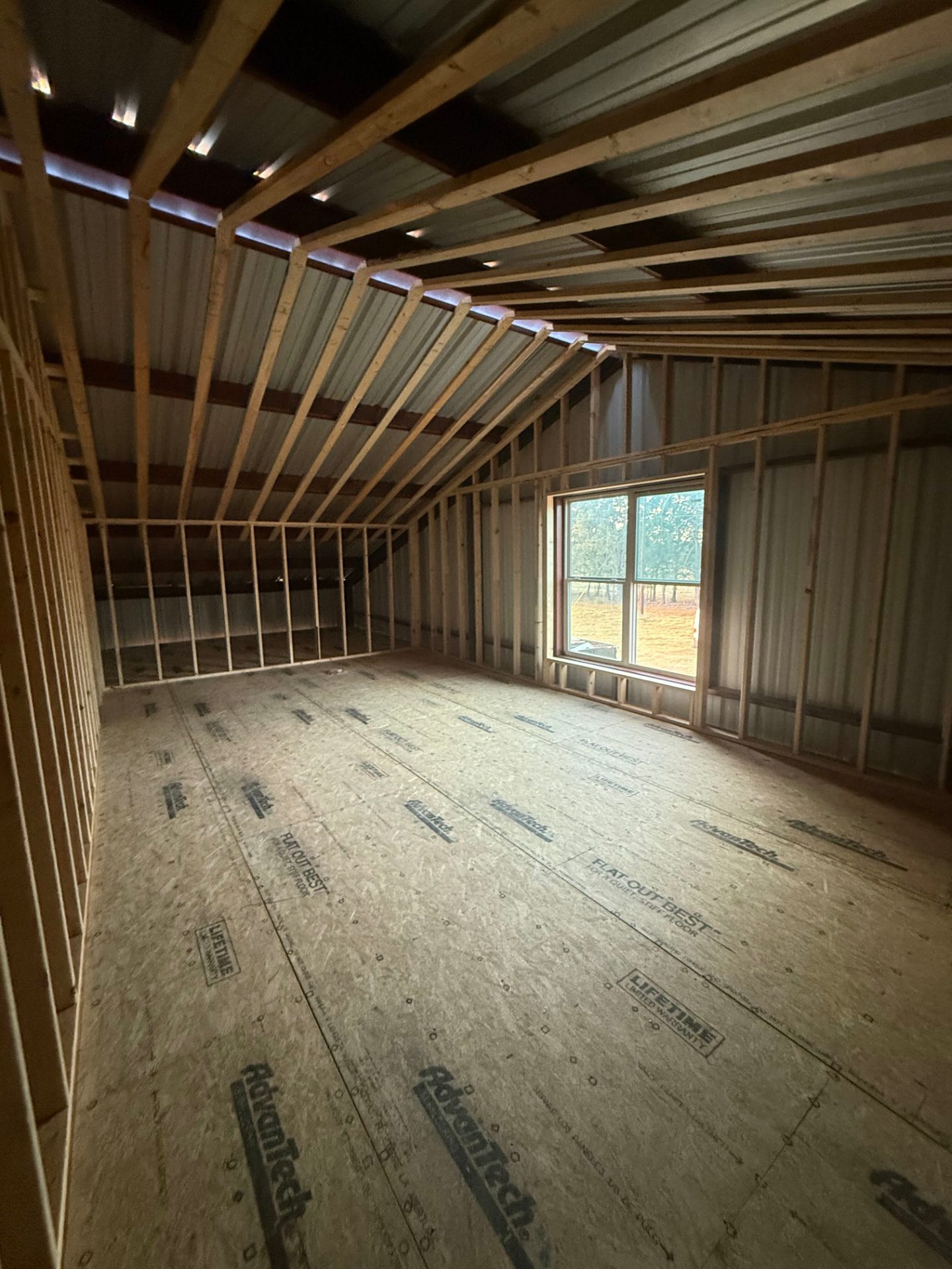 Framed loft room inside a barndominium with vaulted rafters and a new window