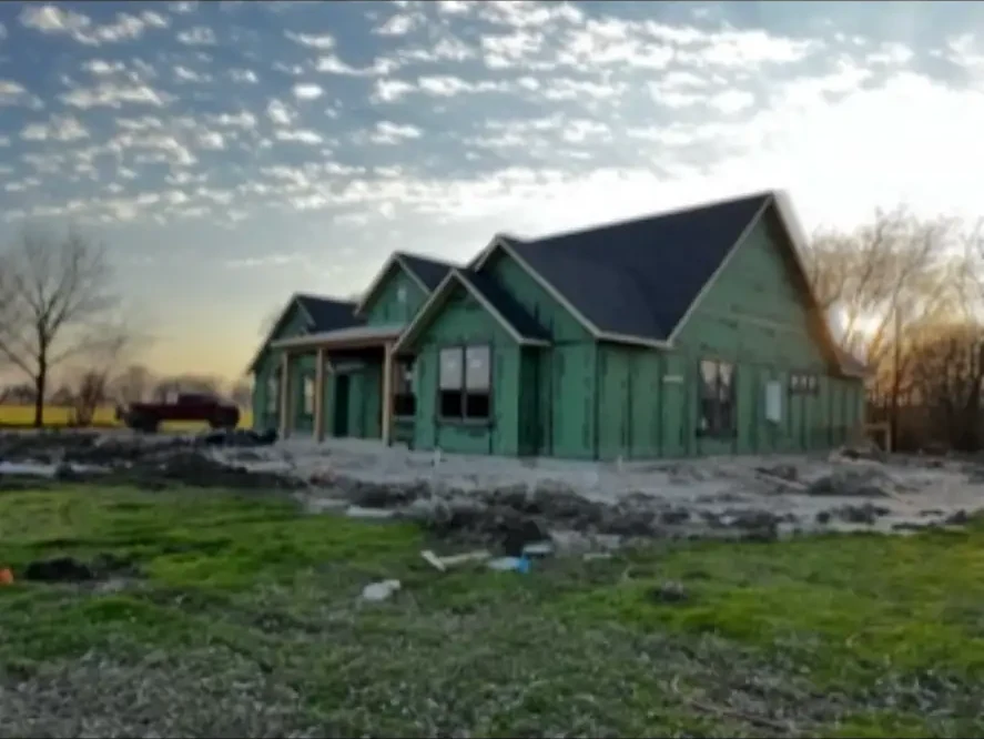 Custom home exterior sheathed and roofed at sunset on an open Texas lot